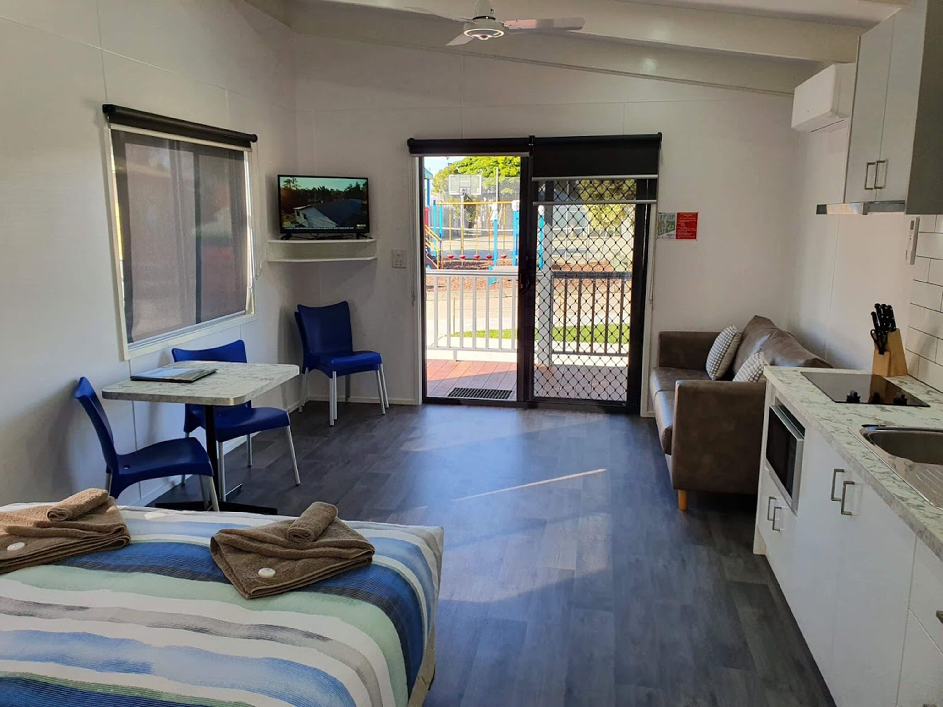 A modern room with a bed, a desk, a chair, a sofa, a TV, and a kitchen area.