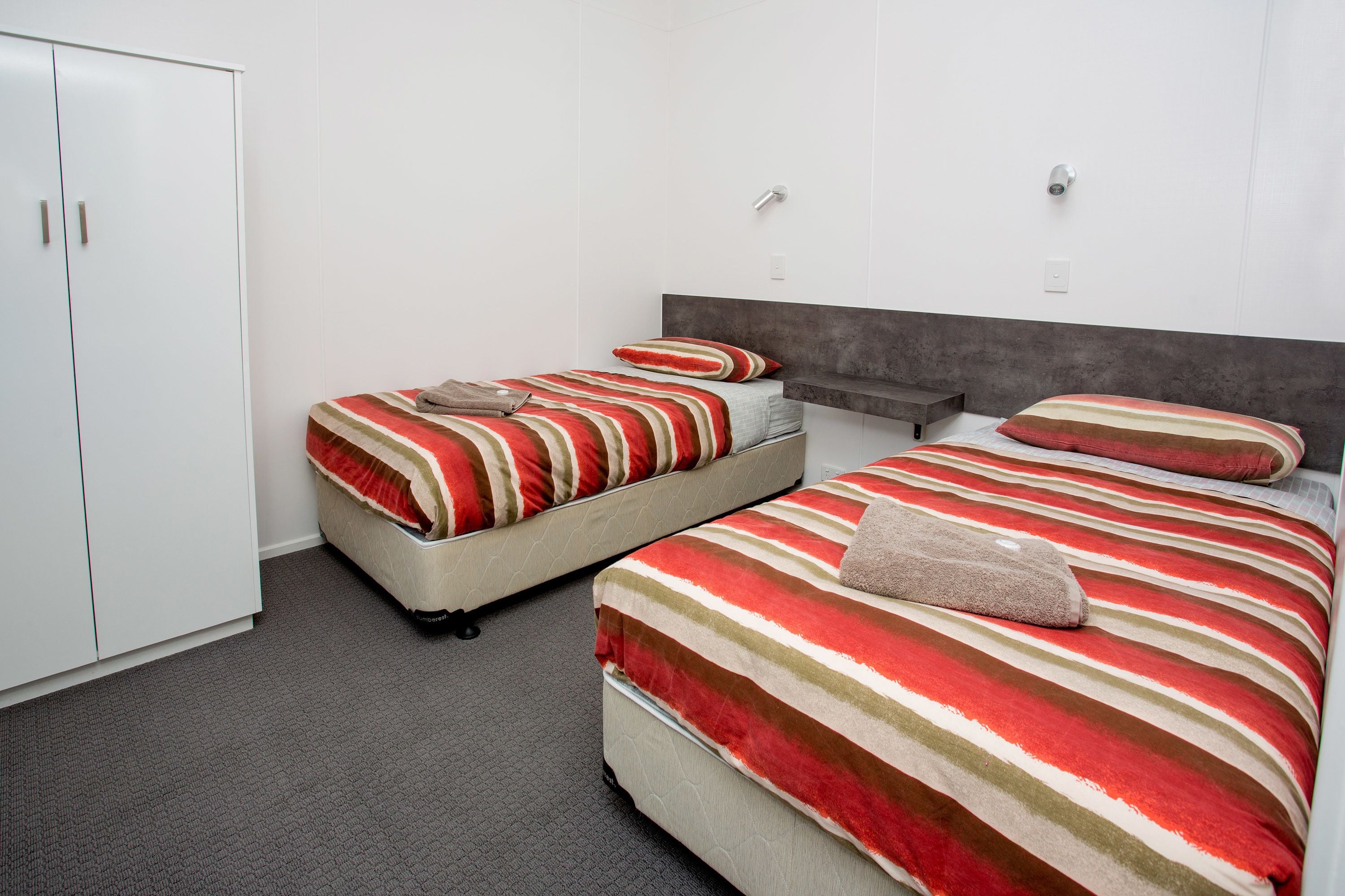 Quarto de hotel com duas camas, um guarda-roupa e um tapete cinza.