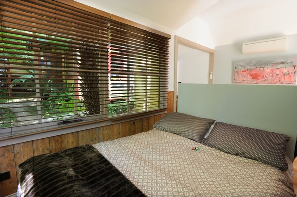 A bedroom with a bed, wooden blinds, a green wall, and a painting.