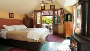 A bedroom with a bed, a wooden dresser, a television, and a fireplace. - Como Cottages Accommodation (Olinda)