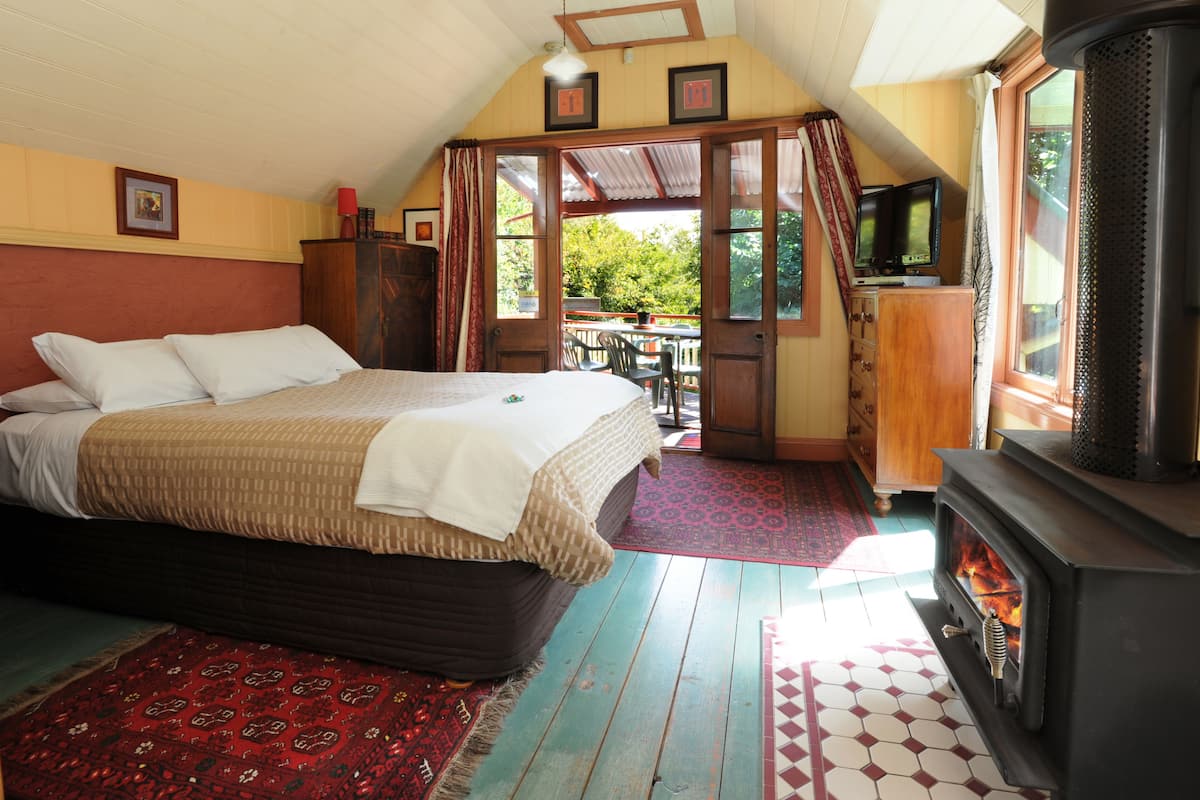 A bedroom with a bed, a wooden dresser, a television, and a fireplace.