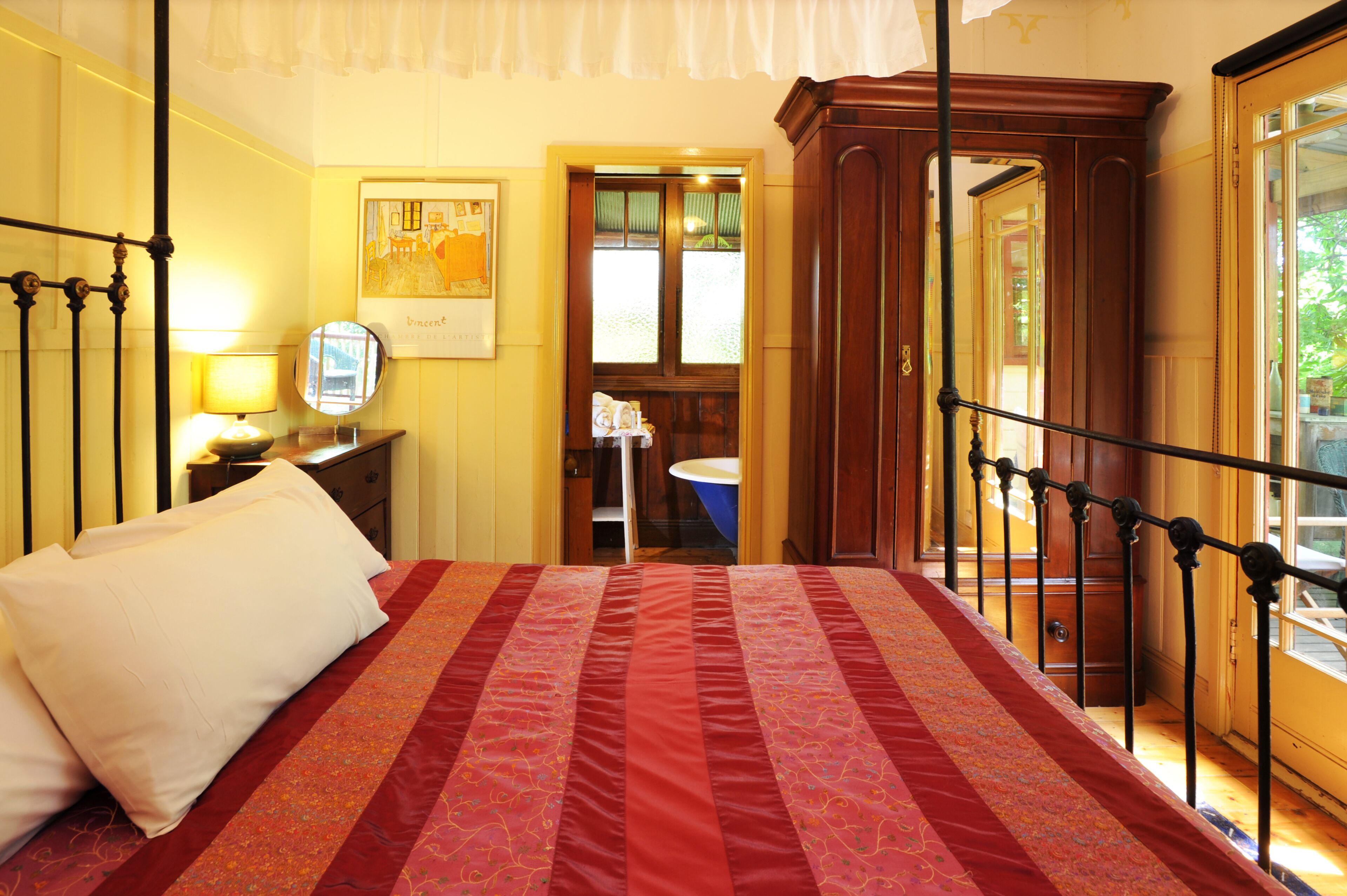 A bed with a red and white bedspread, a bedside table with a lamp, and a mirror on the wall.