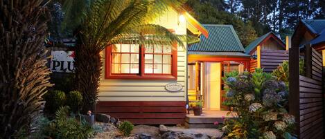 Una cabaña acogedora con fachada de madera, un porche y un letrero que dice "Caretaker's Cottage".