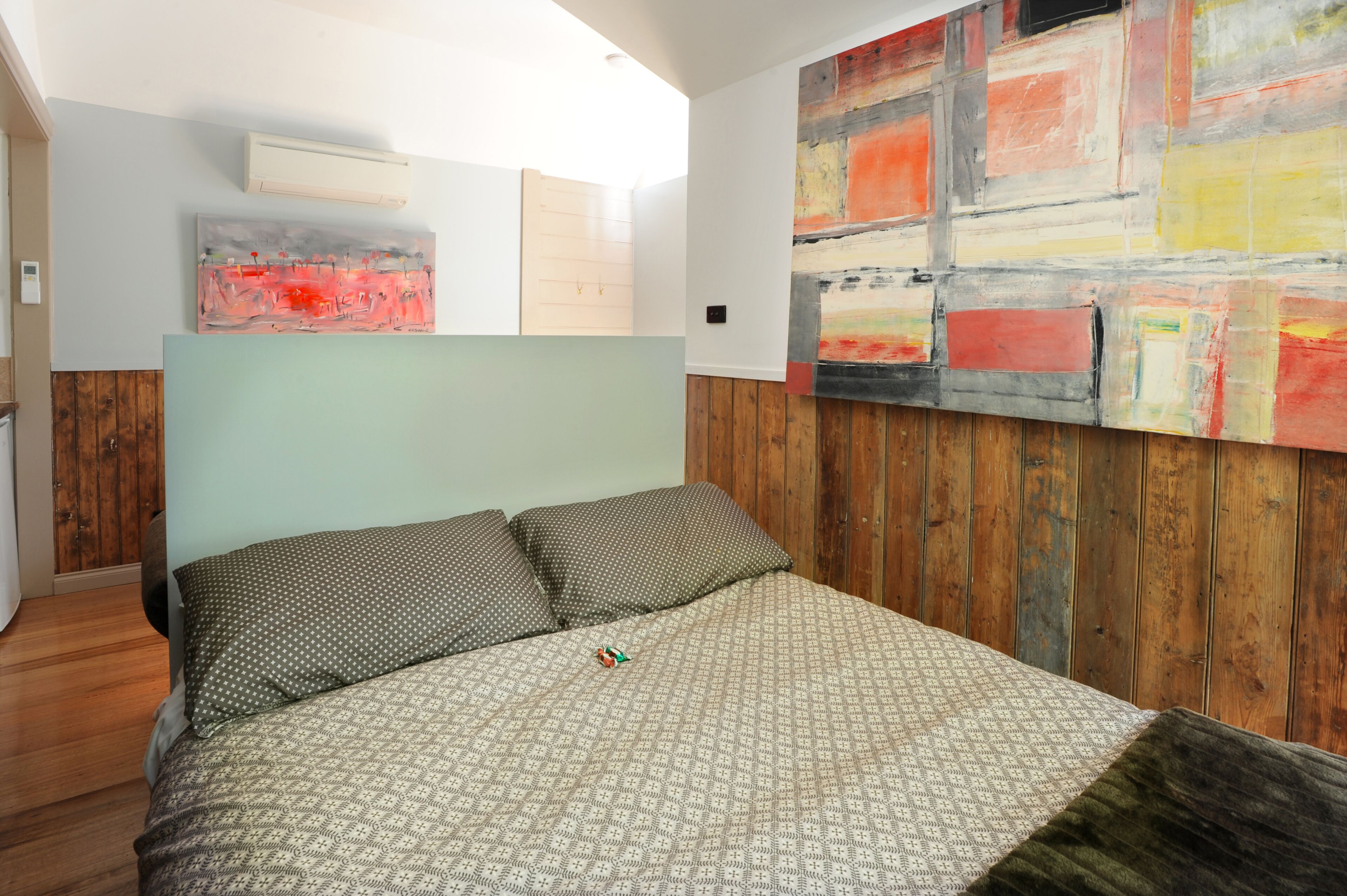 Un dormitorio con cama, paneles de madera en la pared y arte abstracto.