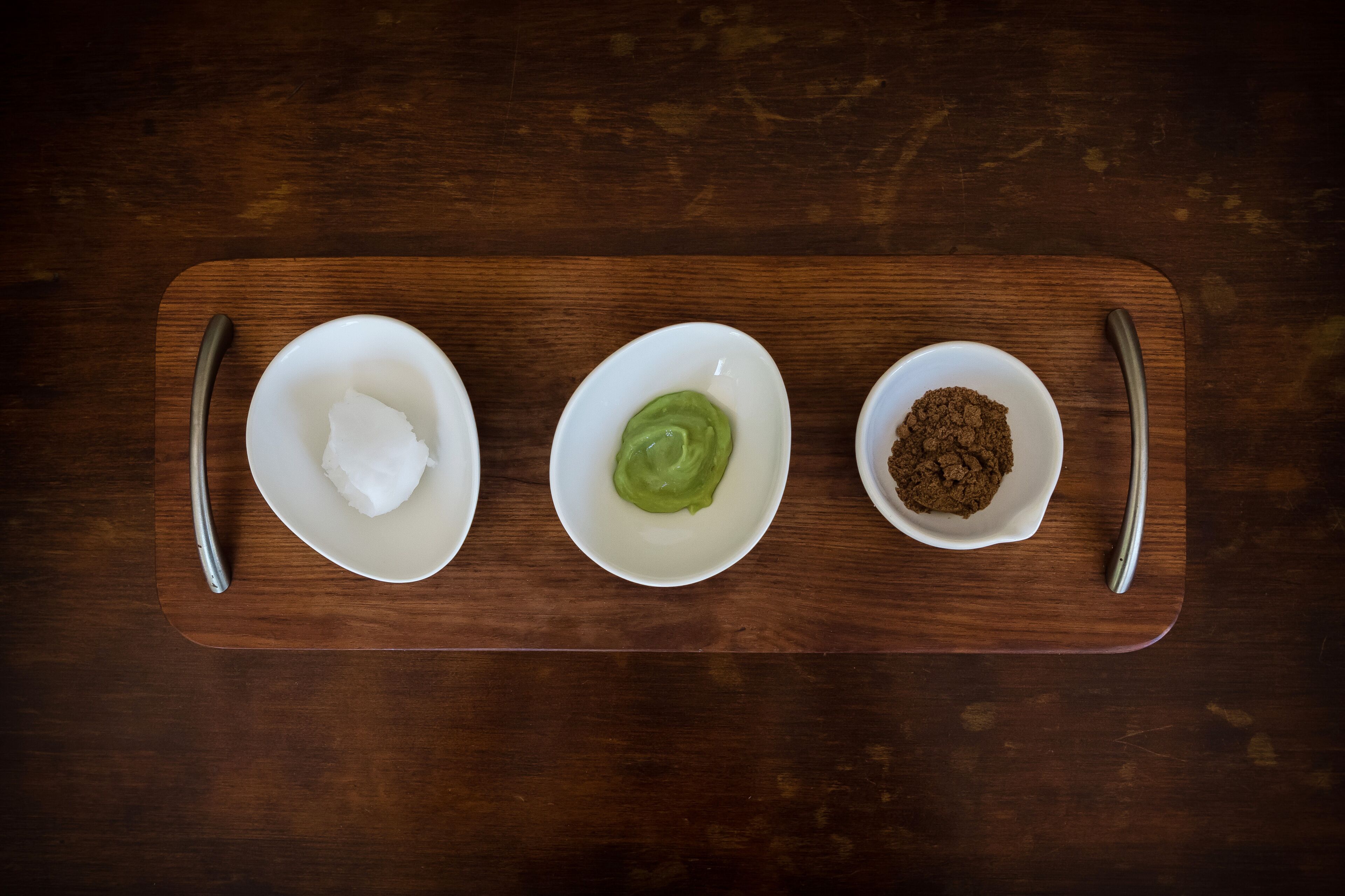 Three white bowls on a wooden tray with spoons on either side.