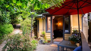 A wooden deck with a red umbrella, a table, and potted plants. - Como Cottages Accommodation (Olinda)