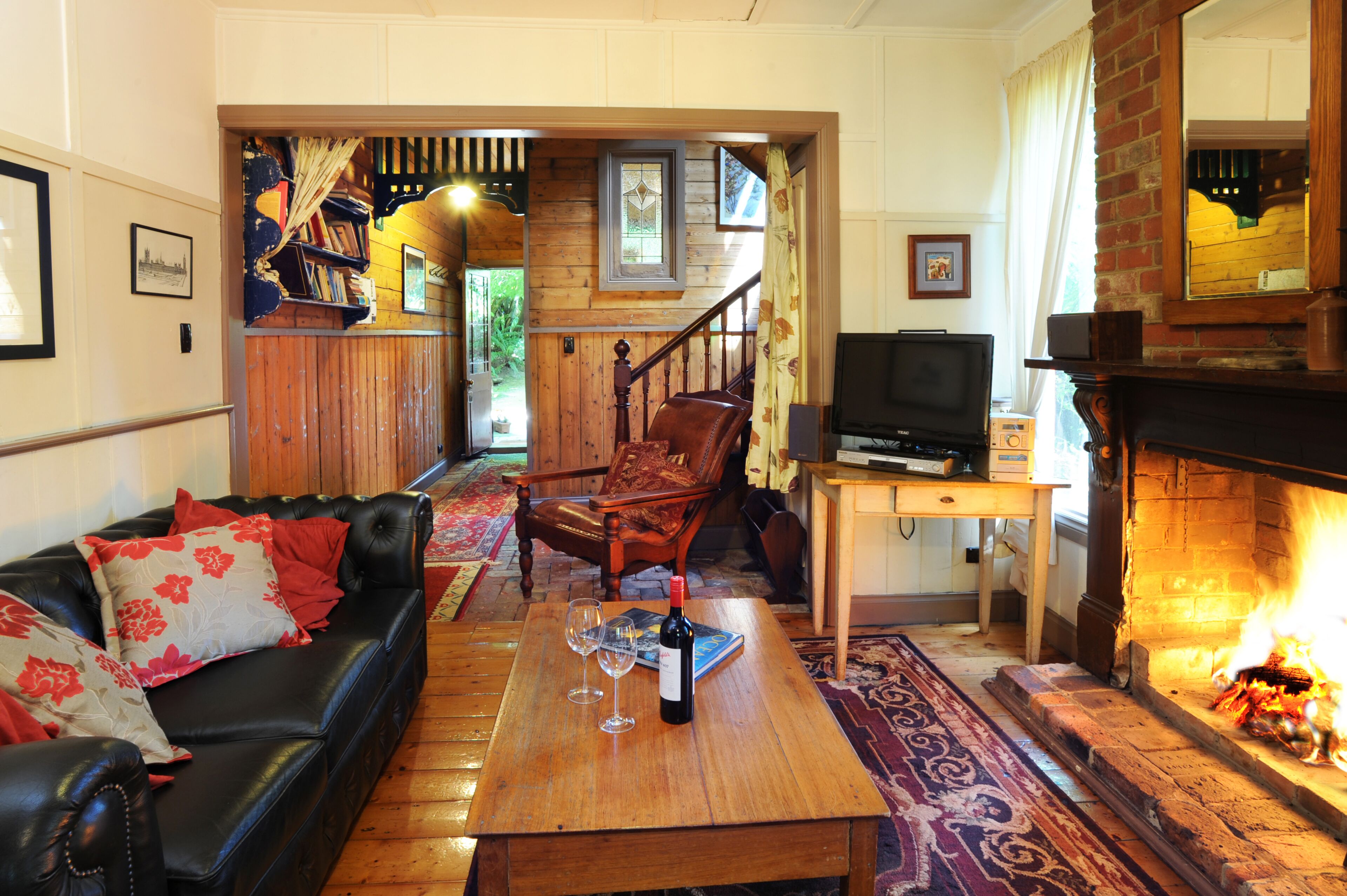 A cozy living room with a fireplace, a leather sofa, a wooden coffee table with wine glasses, and a television.