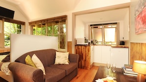 A cozy living room with a brown sofa, a dining table with a fruit platter, and a kitchen area with a microwave and coffee maker. - Como Cottages Accommodation (Olinda)