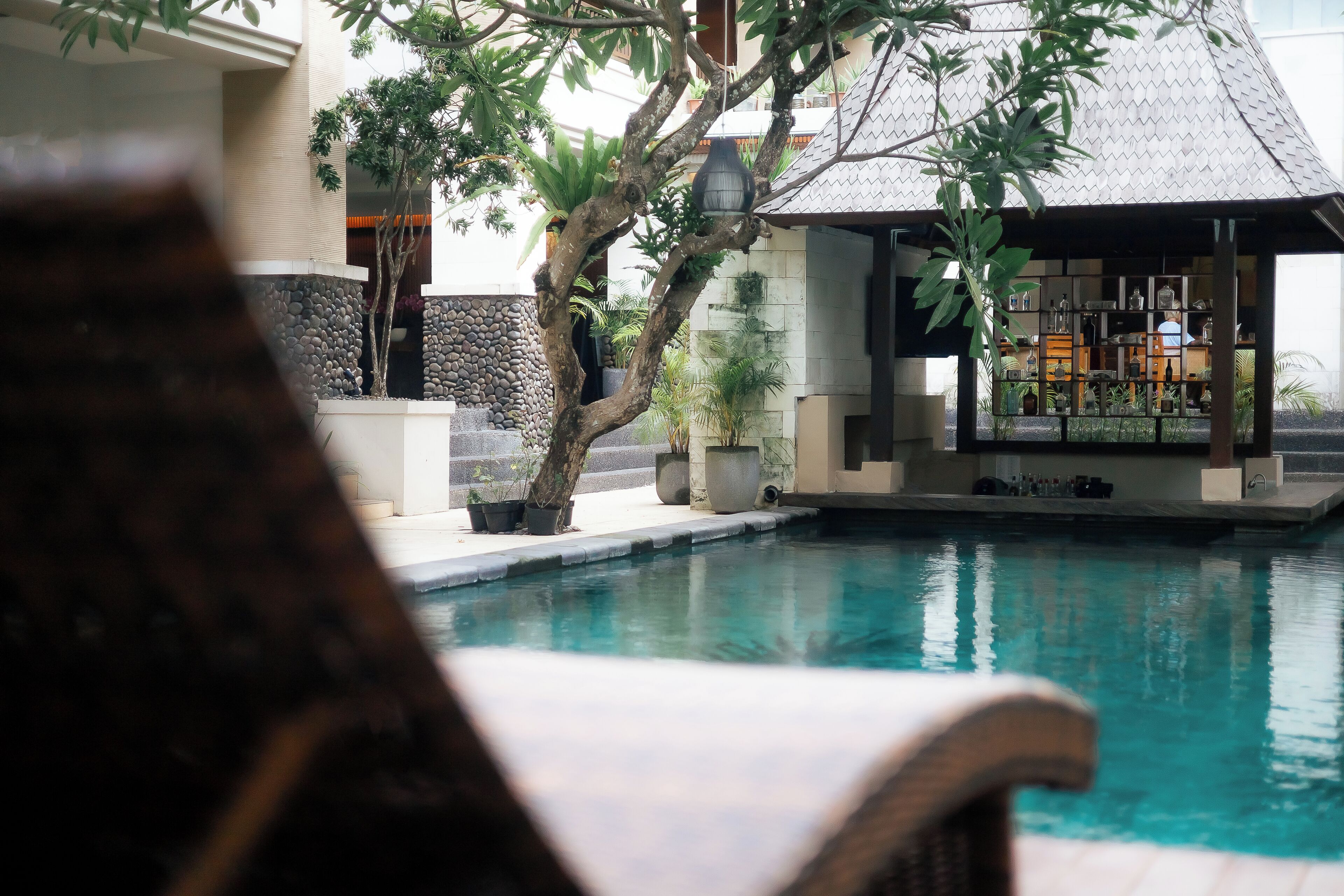 A pool area with a covered seating area, stone walls, and potted plants.