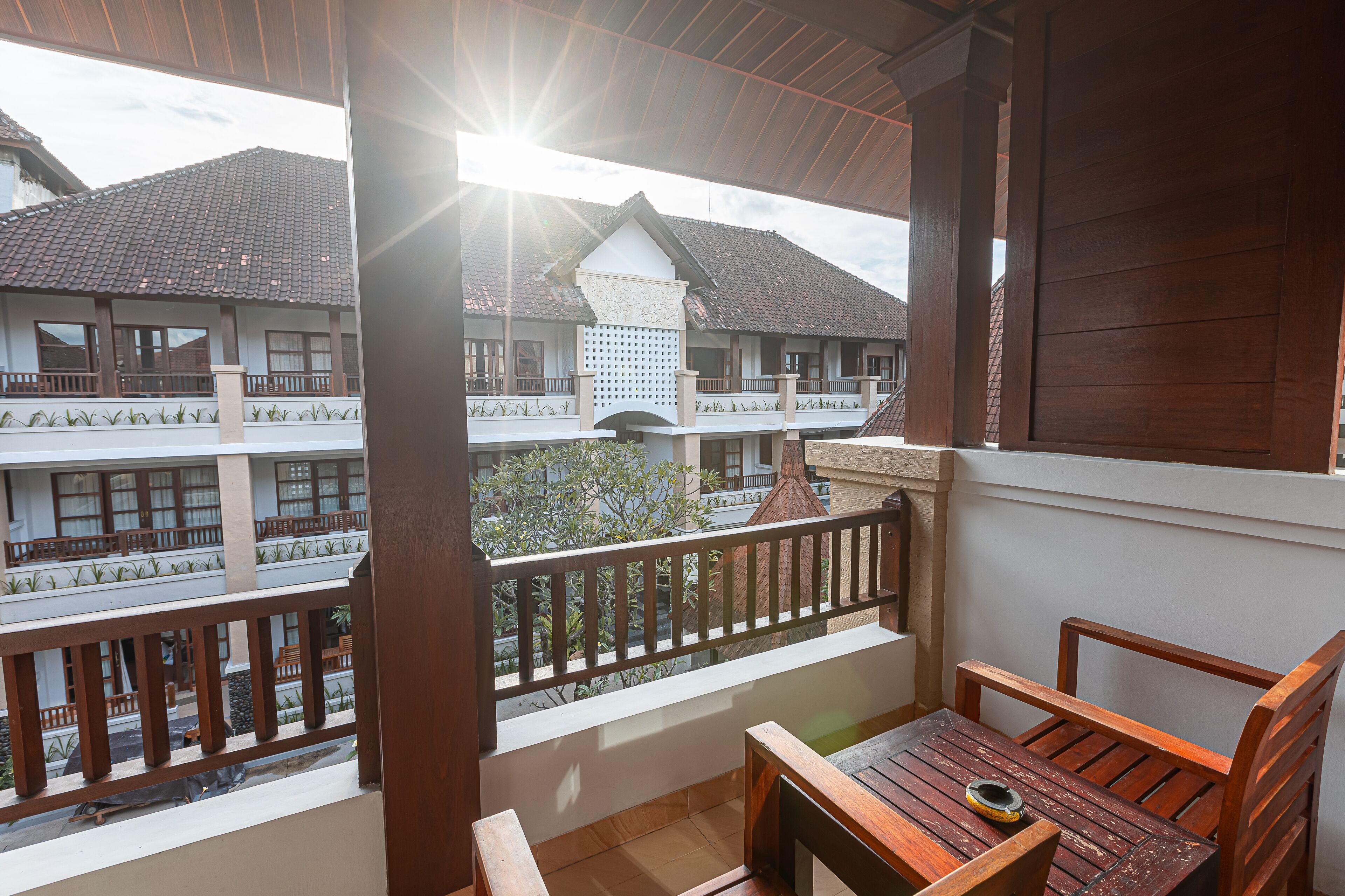 A balcony with wooden furniture, a view of a building with multiple floors, and a clear sky.