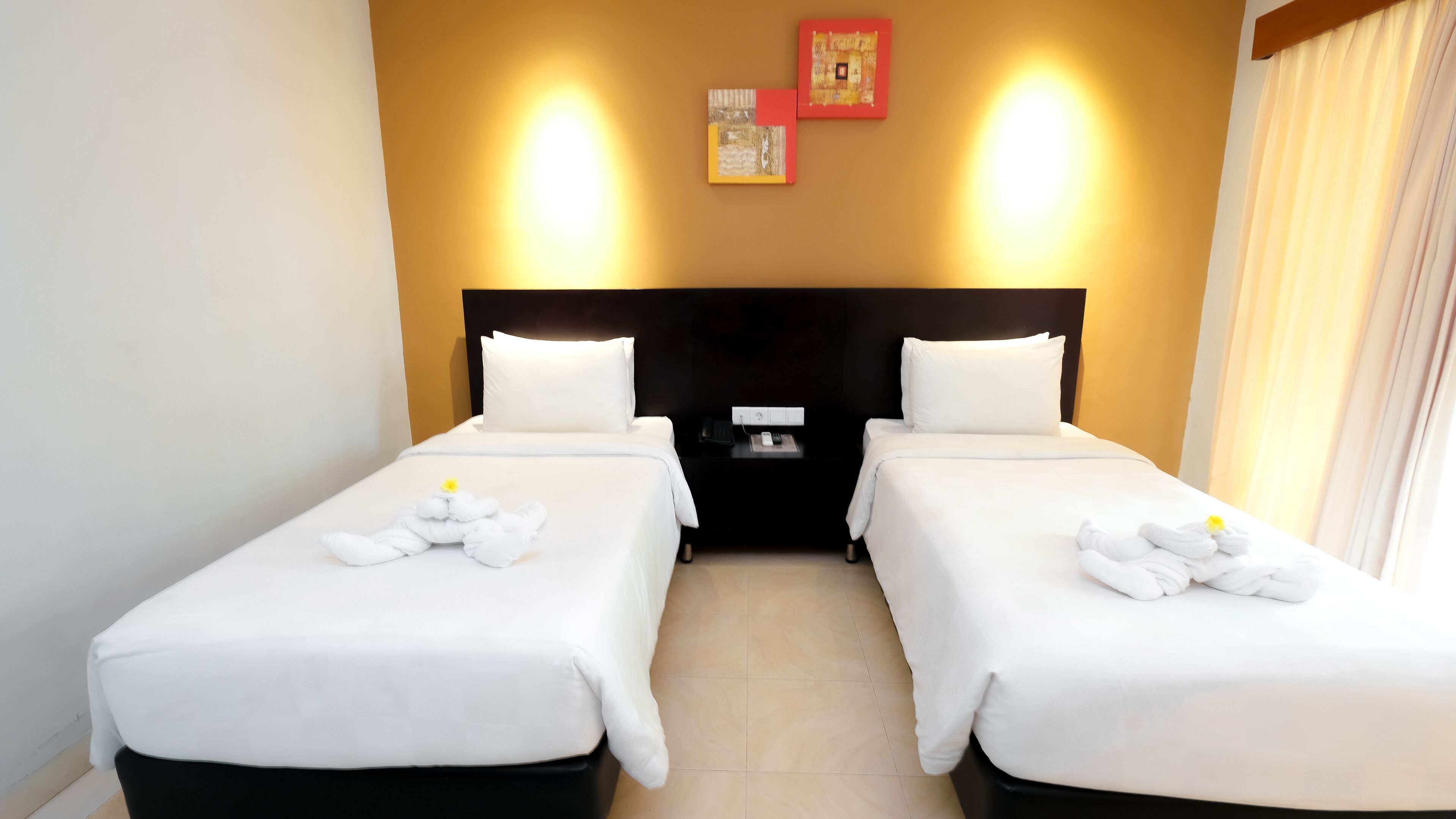 A hotel room with two beds, a nightstand, a wall-mounted light, and a small picture.