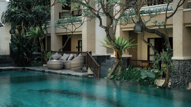 A pool area with a lounge chair and a stone wall. - Fourteen Roses Beach Hotel (Legian)