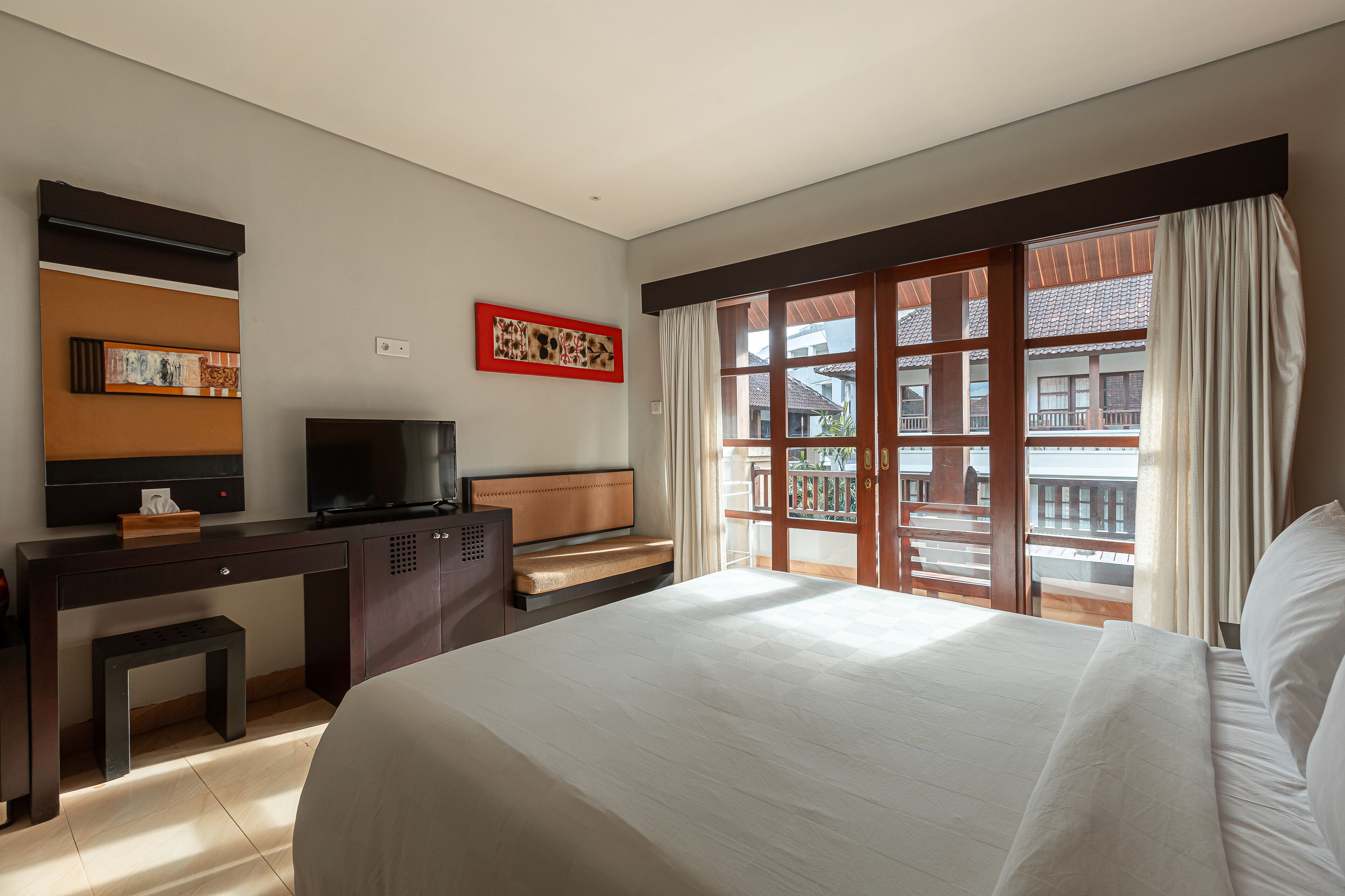 Quarto de hotel com uma cama, uma mesa com televisão, uma mesinha e uma janela com vista para edifícios.