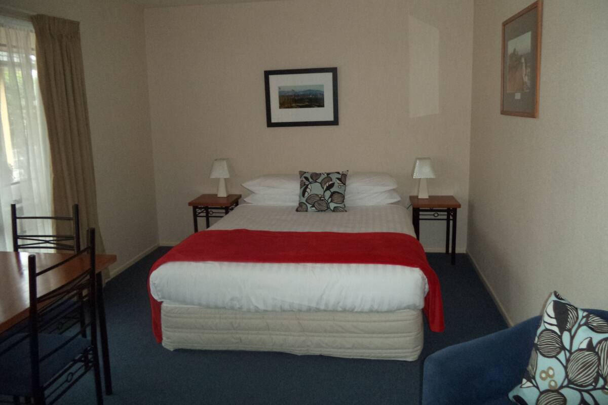 A hotel room with a bed, two bedside tables, a chair, a desk, and a framed picture on the wall.