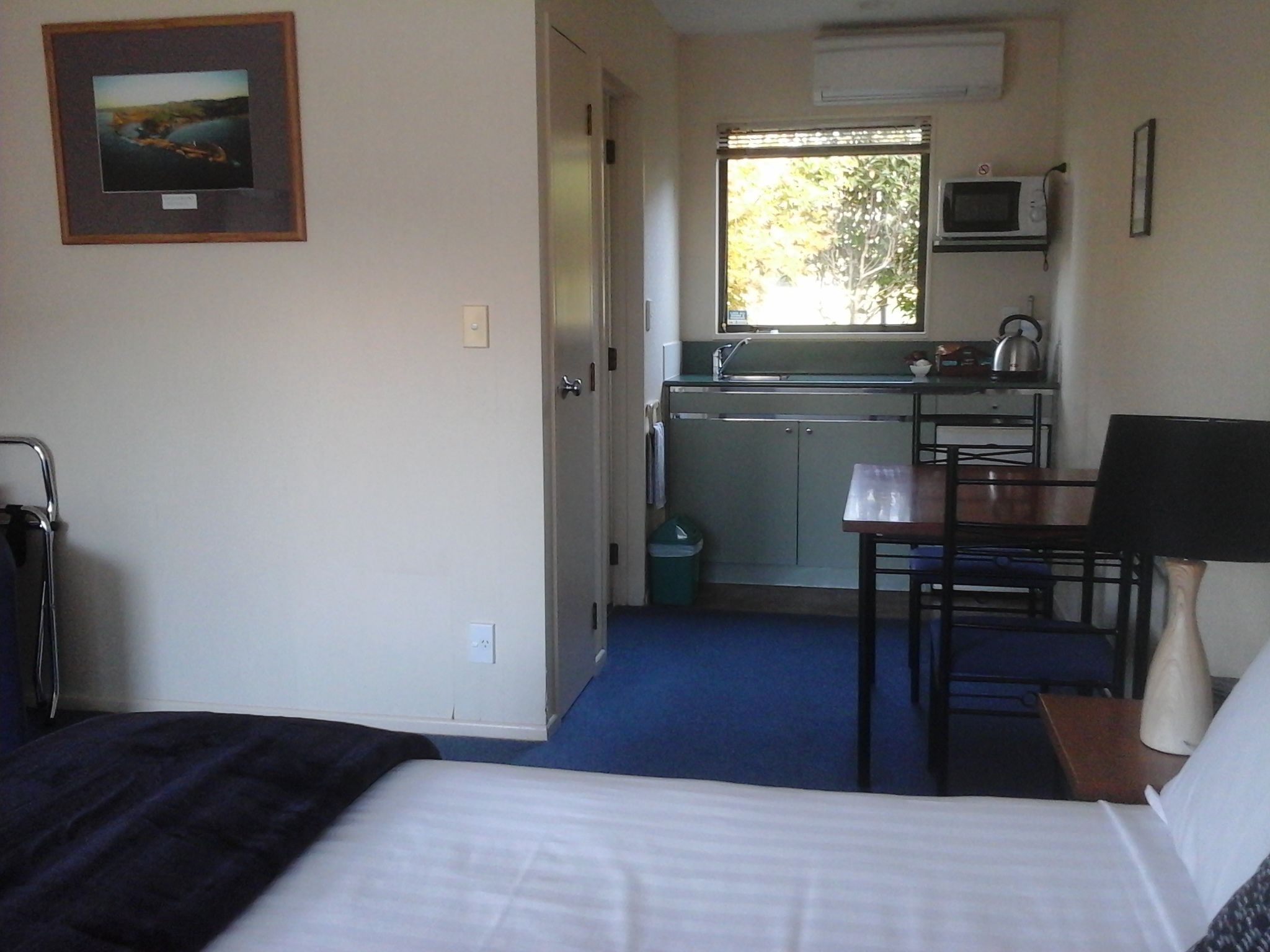 Habitación de hotel compacta con cama, pequeño escritorio, silla, microondas y kitchenette.
