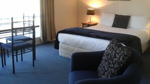A hotel room with a bed, a chair, a nightstand with a lamp, and a window with curtains. - South Park Motel (Masterton)