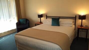 Een hotelkamer met een groot bed, twee nachtkastjes met lampen, een stoel en een raam met gordijnen.