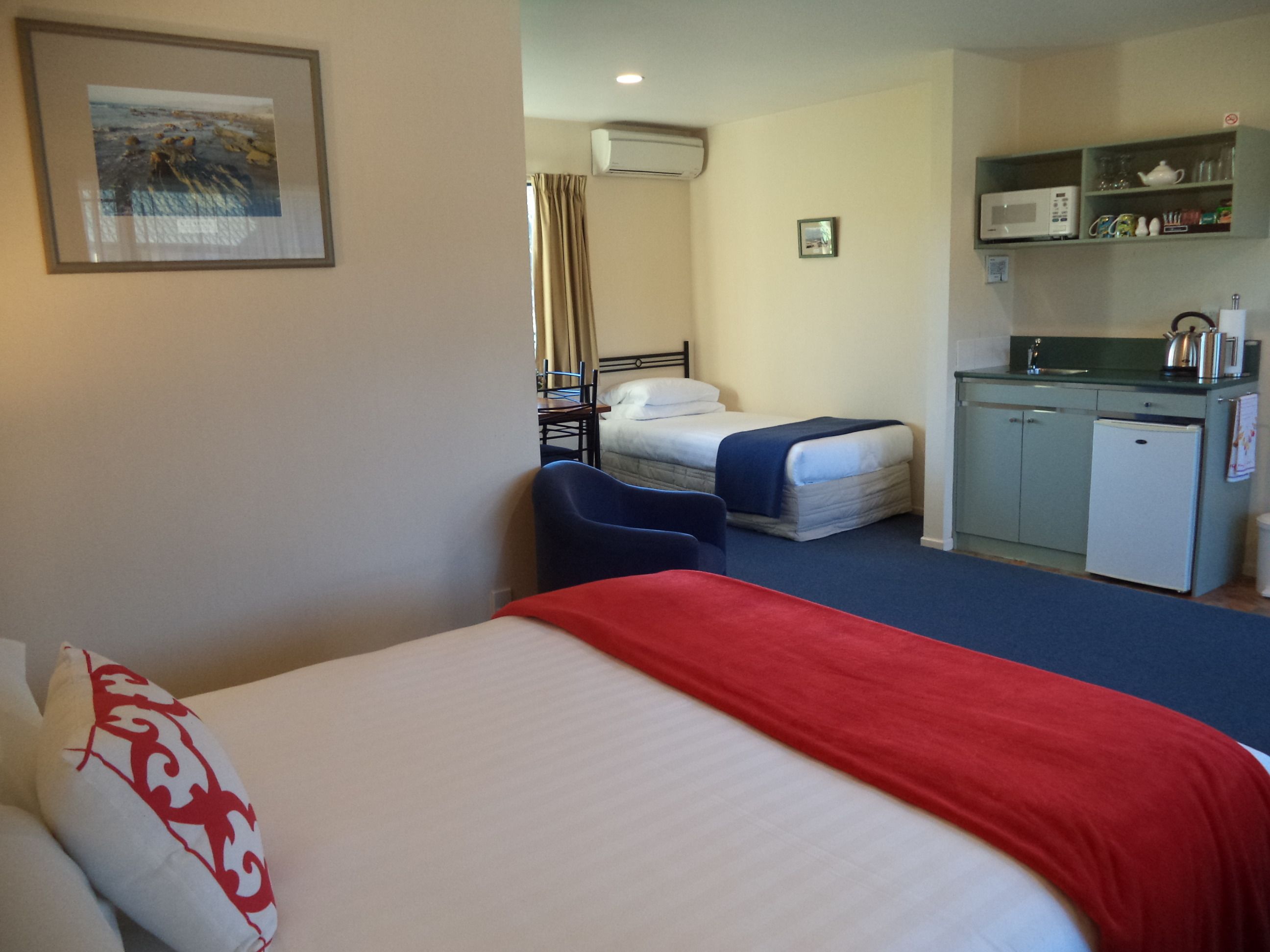 A hotel room with a bed, a desk, a chair, a kitchenette, and a bathroom.
