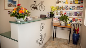 A reception desk with a flower arrangement, a bicycle wall decoration, a bookshelf with books, and a blue vase with umbrellas. - South Park Motel (Masterton)