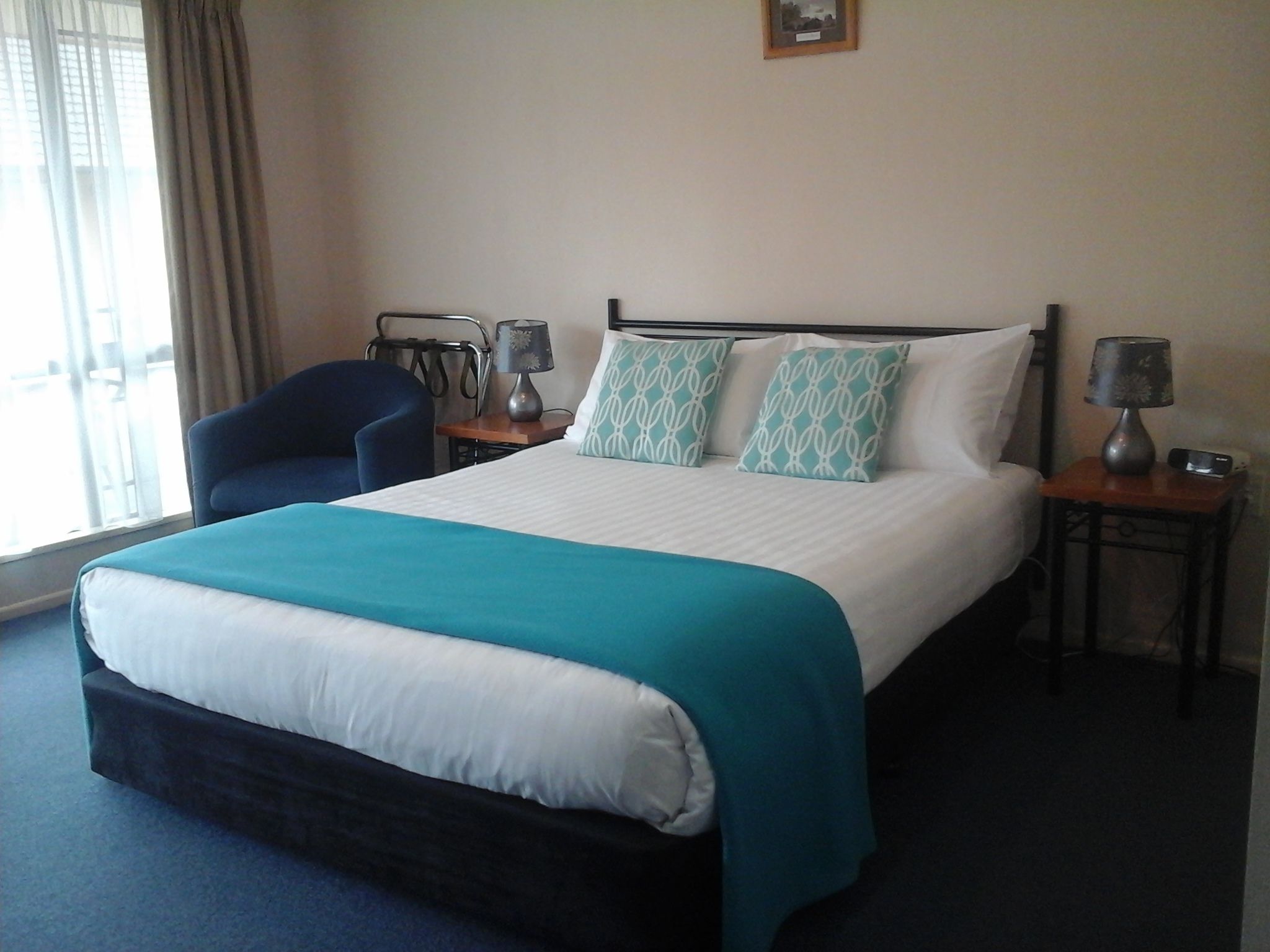 A hotel room with a bed, two bedside tables, a chair, and a window with curtains.