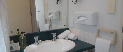 A bathroom with a white sink, two faucets, a mirror, a towel rack, and a hairdryer mounted on the wall.