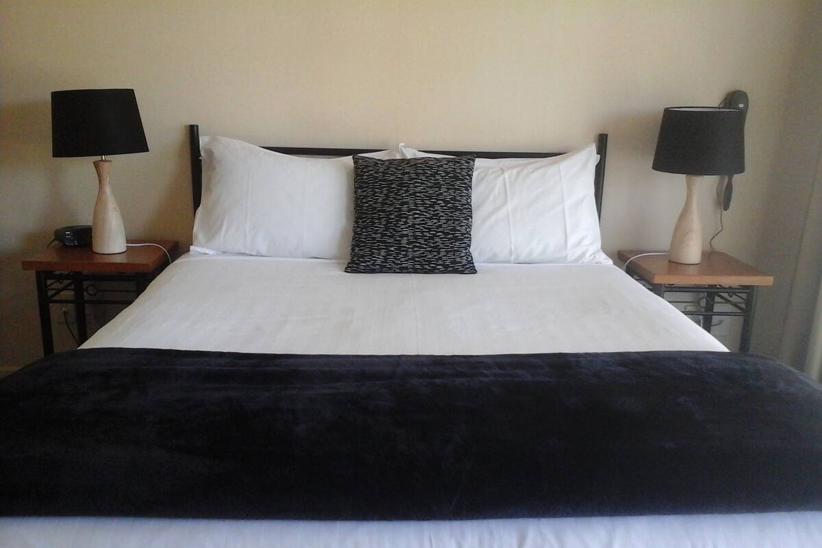 A neatly made bed with white and black bedding, two bedside lamps, and a bedside table with a lamp.