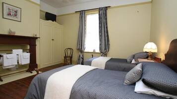 A bedroom with two beds, a wooden dresser, a chair, a window with curtains, and a wall-mounted TV.