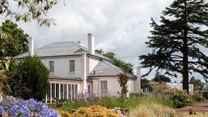 A two-story house with a white exterior, surrounded by a garden with various plants and flowers. - Fitzpatrick's Inn (Westbury)