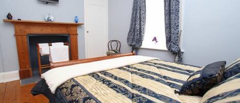 A bedroom with a bed, a fireplace, a television, and a window with curtains.