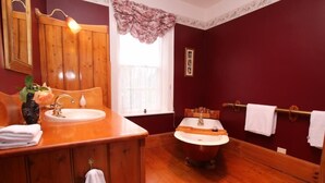 A bathroom with wooden vanity, a freestanding bathtub, and a window with a floral curtain.
