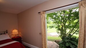 A hotel room with a bed, a bedside lamp, and a view of a garden through an open door. - Fitzpatrick's Inn (Westbury)