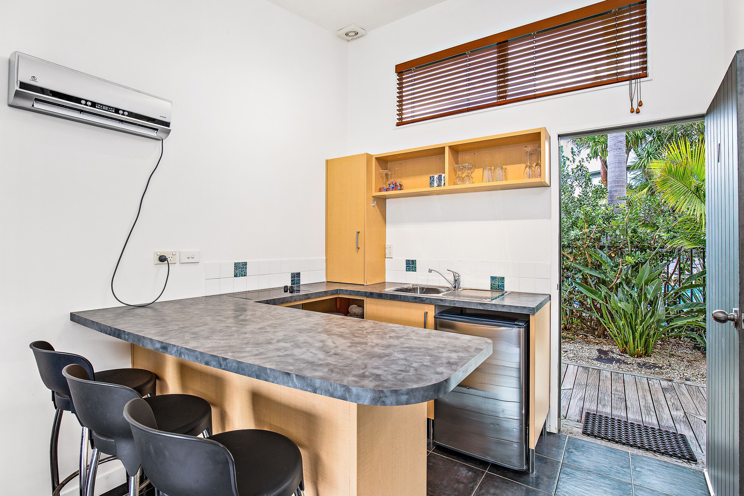 A modern kitchen with a central island, bar stools, a built-in oven, and a window with blinds.
