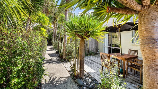 A wooden deck with a table and chairs, surrounded by various tropical plants and a pathway. - Waipu Cove Resort (Waipu)