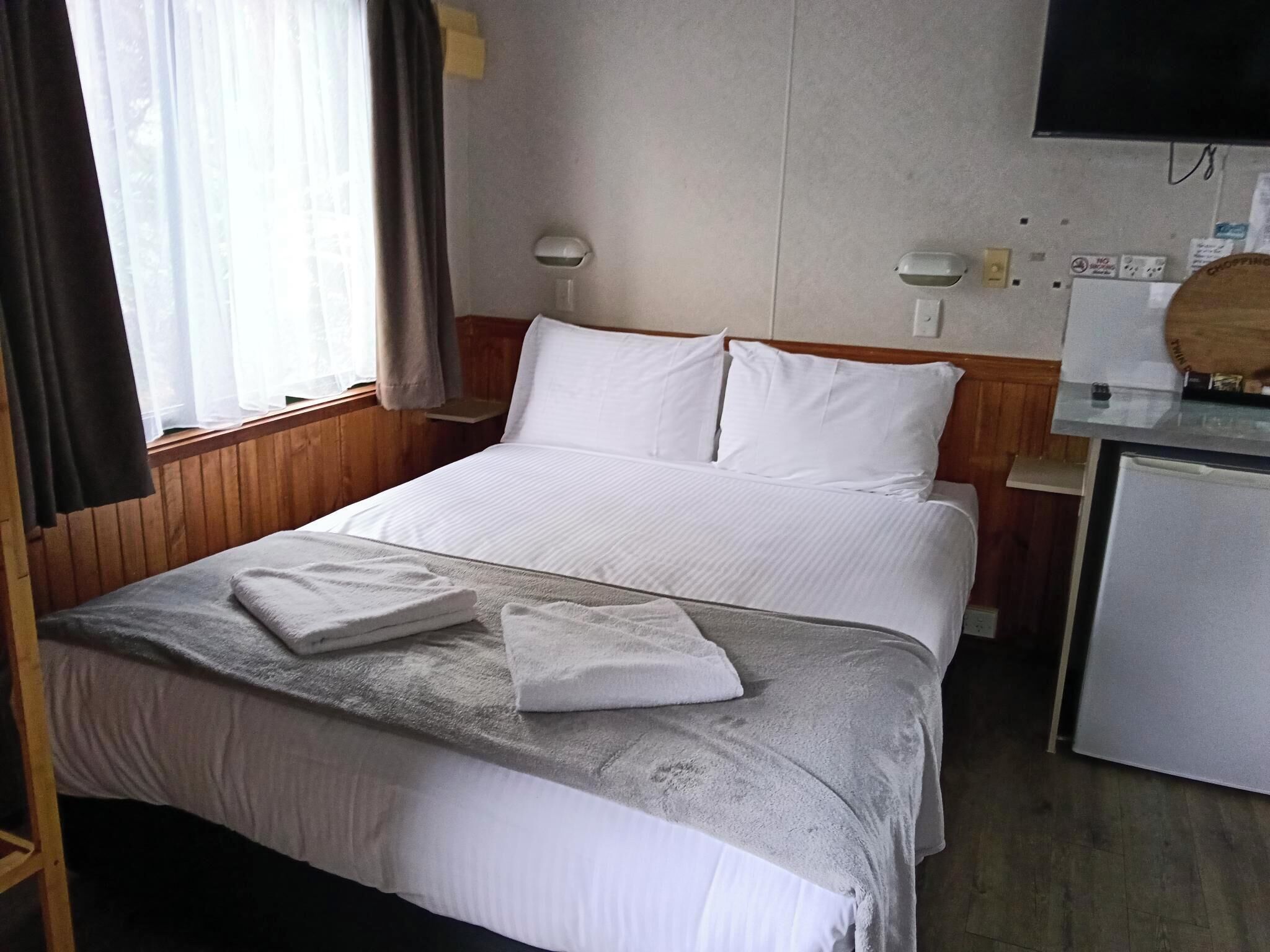 Una camera d'albergo con un letto, una scrivania, una sedia, una TV e una finestra con tende.