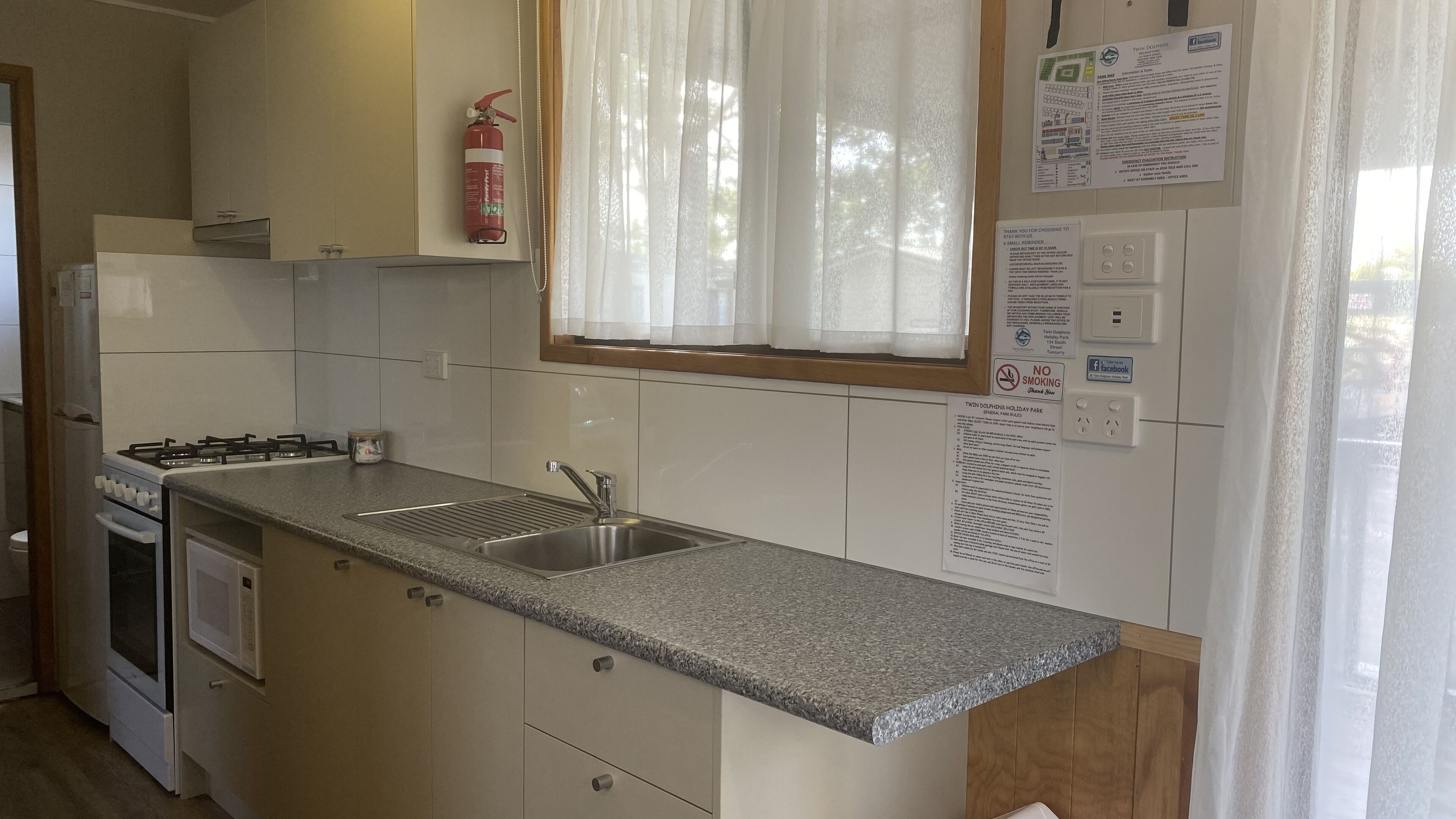 A kitchen with a granite countertop, stainless steel sink, and a gas stove. There is a fire extinguisher mounted on the wall above the sink.