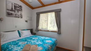 A bedroom with a bed, a window with curtains, a wall-mounted light, and a ceiling fan. - Twin Dolphins Holiday Park (Tuncurry)