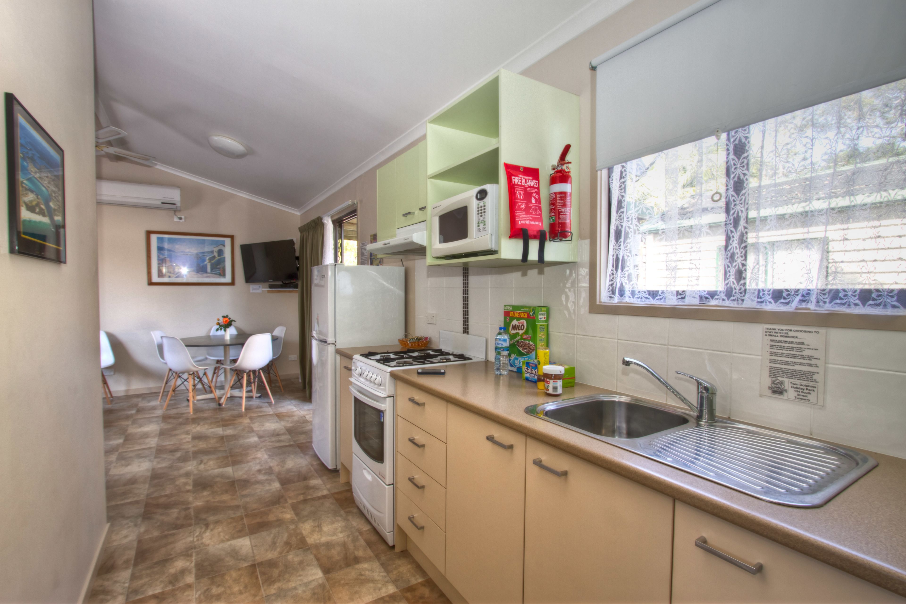 A compact kitchen with a microwave, stove, and sink. There is a dining area with a table and chairs.
