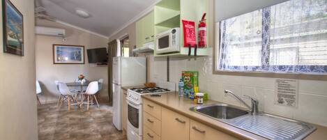 A compact kitchen with a microwave, stove, and sink. There is a dining area with a table and chairs.