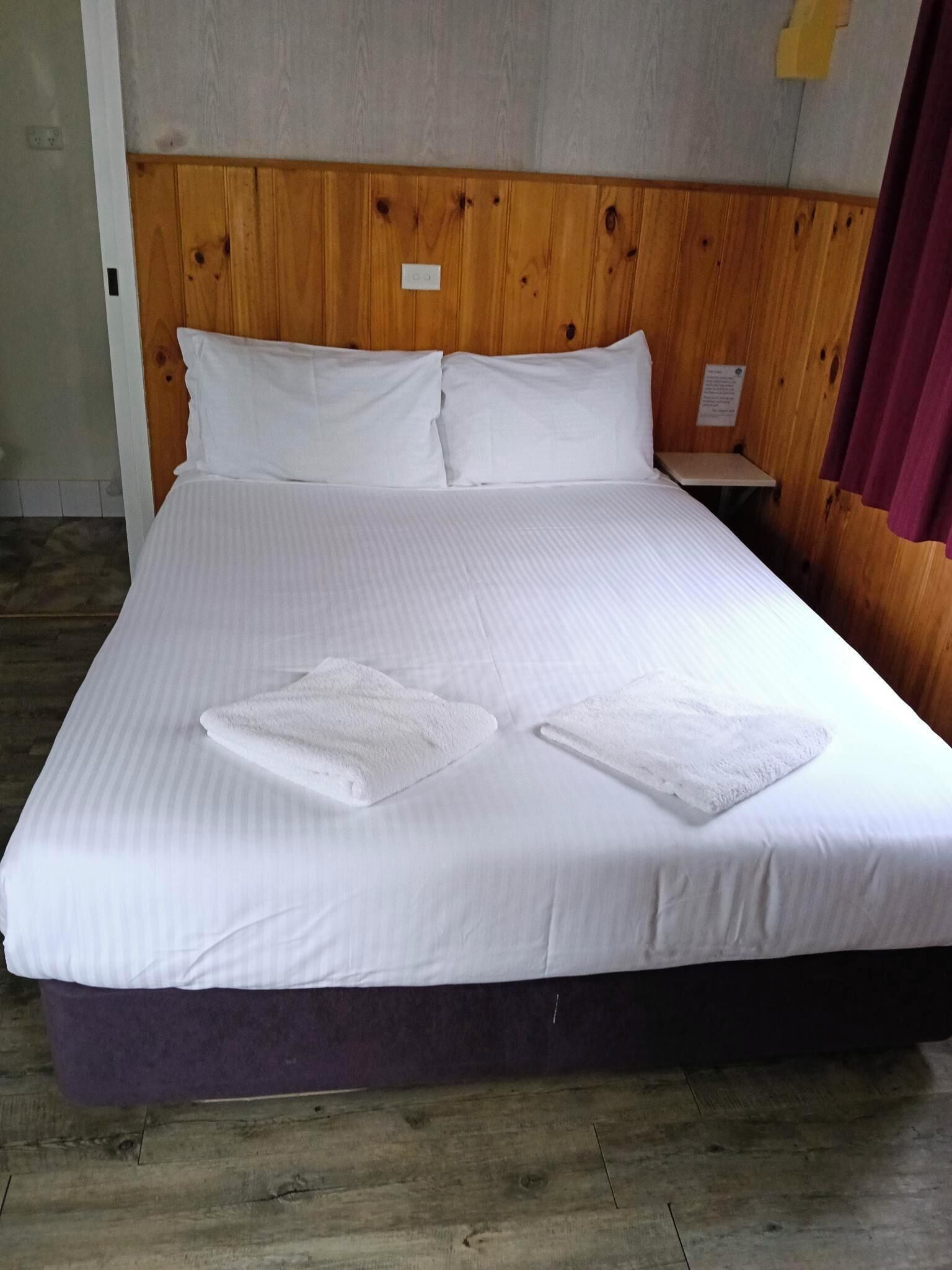 A bed with white linens, two pillows, and two towels.