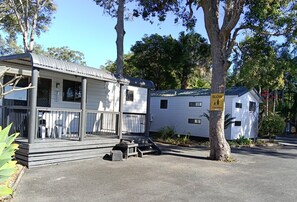 A small, single-story cabin with a porch and a fenced yard. - Twin Dolphins Holiday Park (Tuncurry)