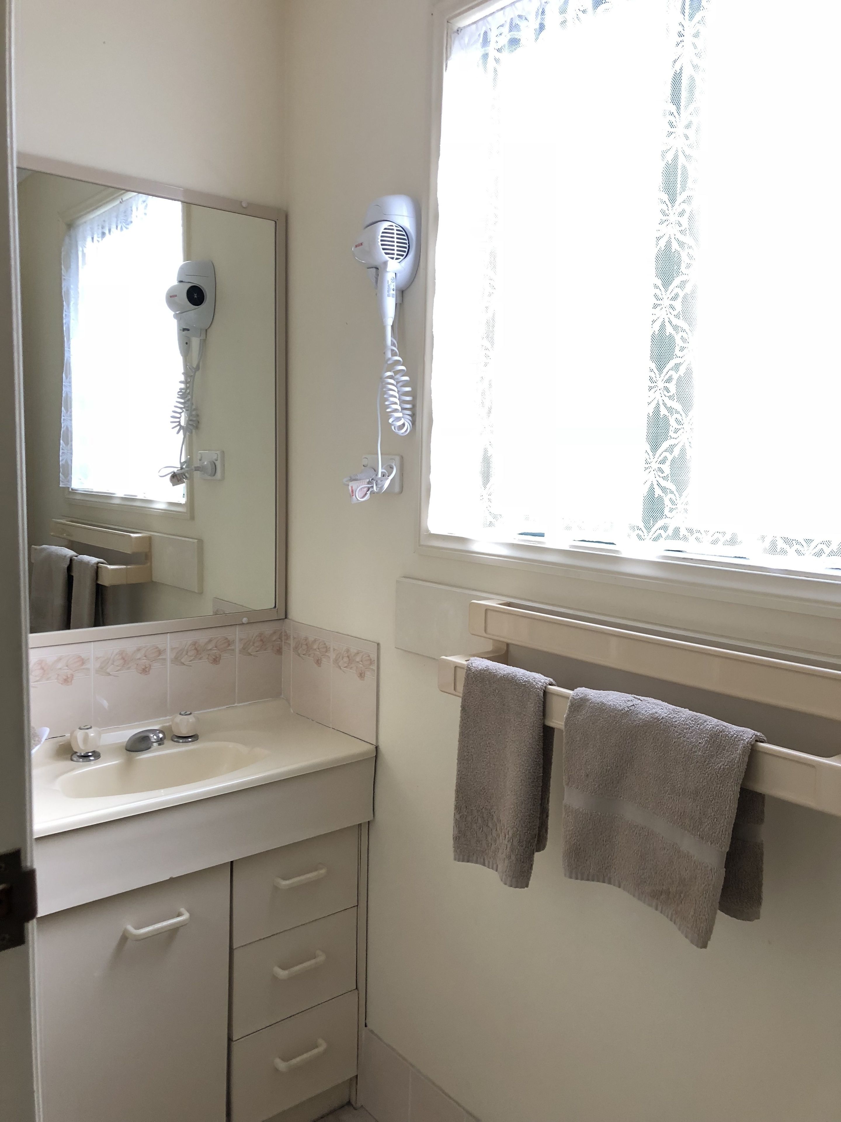 A bathroom with a sink, mirror, towel rack, and a hairdryer mounted on the wall.