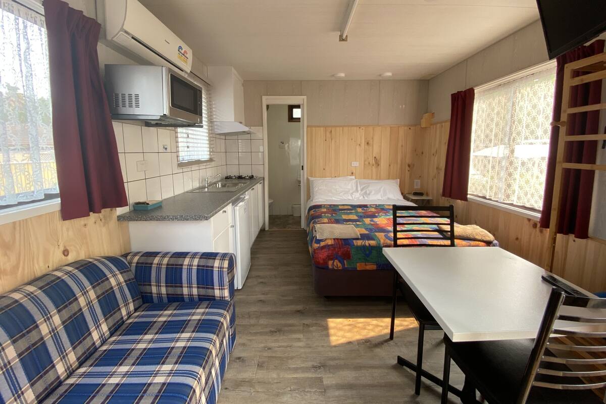A compact room with a kitchenette, a bed, a sofa, and a dining table.
