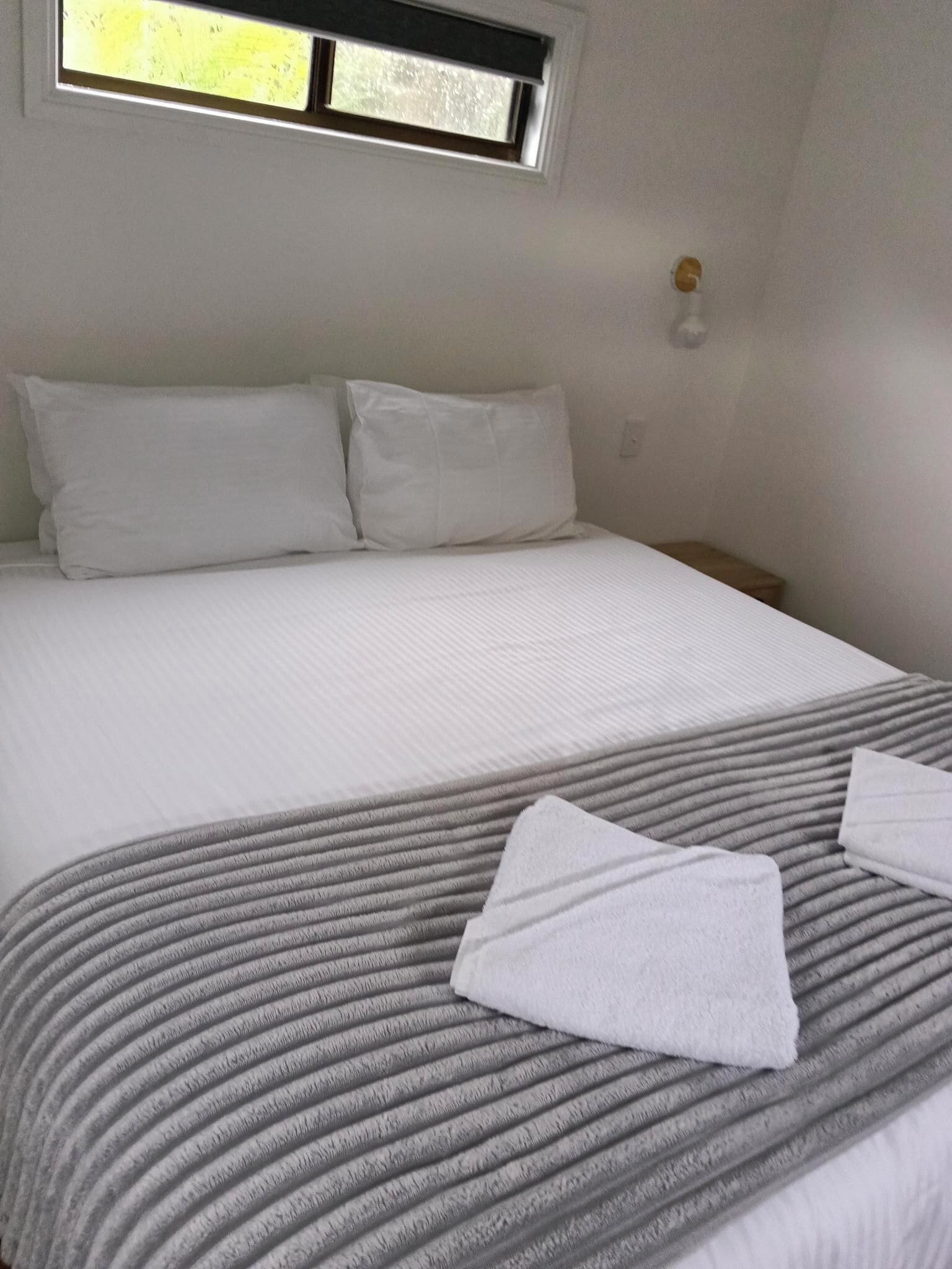 Una cama con ropa blanca, una colcha gris a rayas y dos toallas blancas.