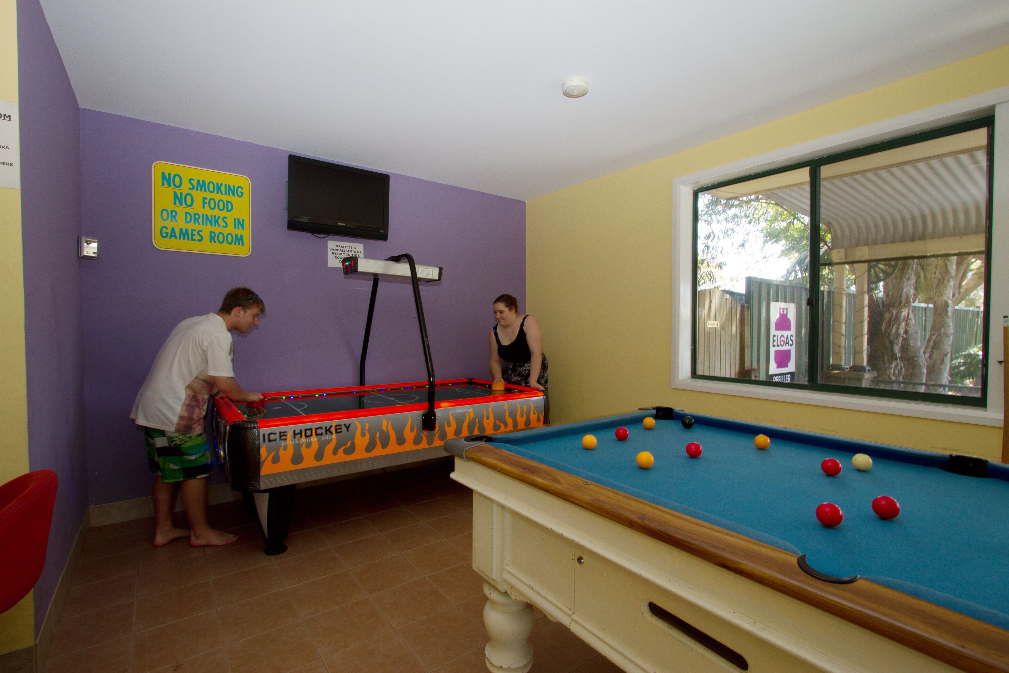A pool table with balls, a pool table with a no smoking sign, and a television on the wall.