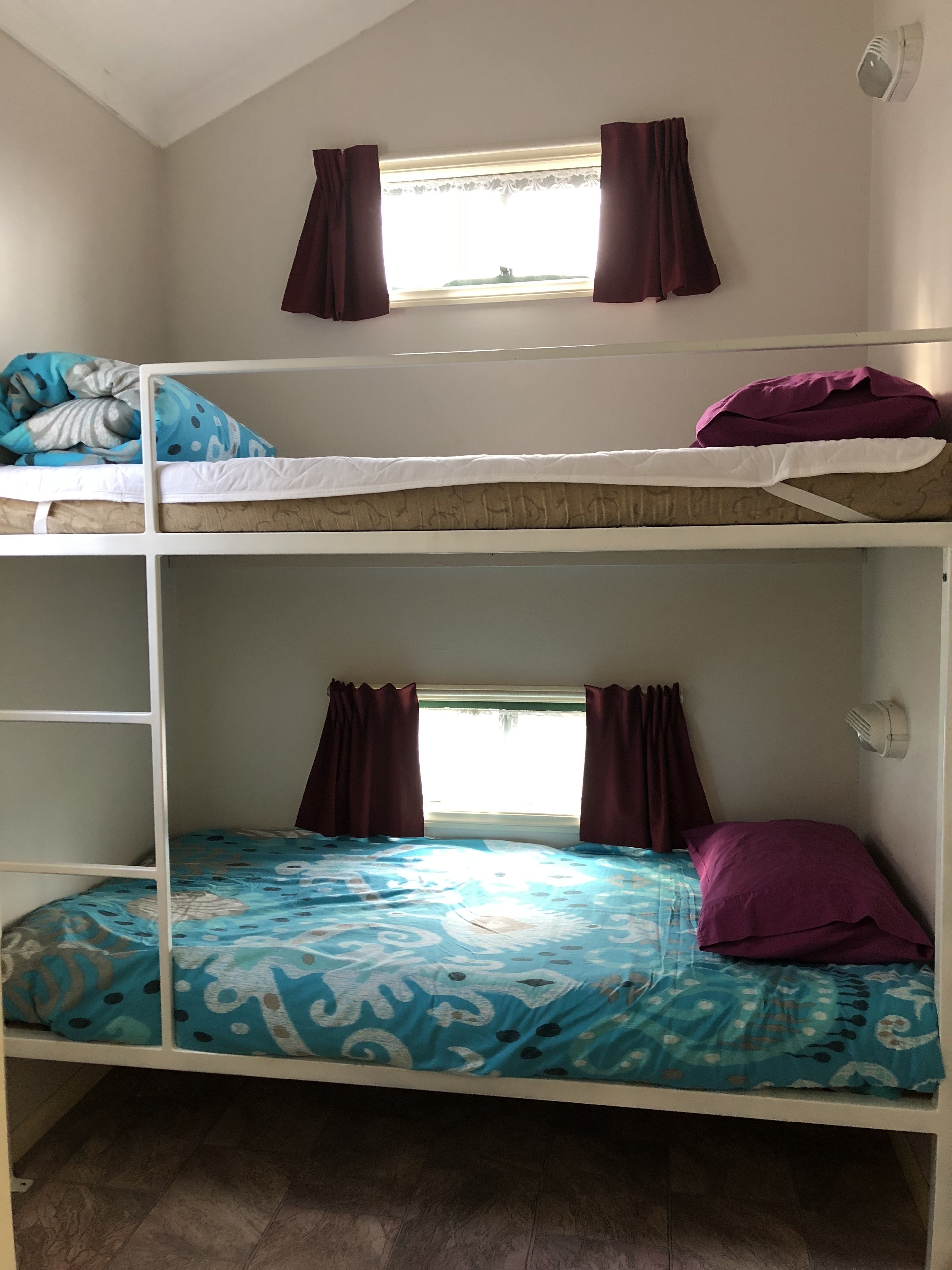 A bunk bed room with a window, curtains, and a wall-mounted fan.