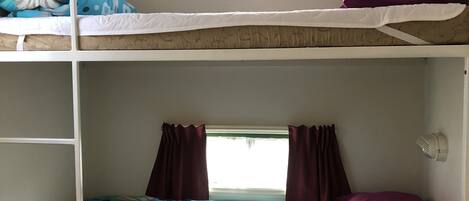 A bunk bed room with a window, curtains, and a wall-mounted fan.