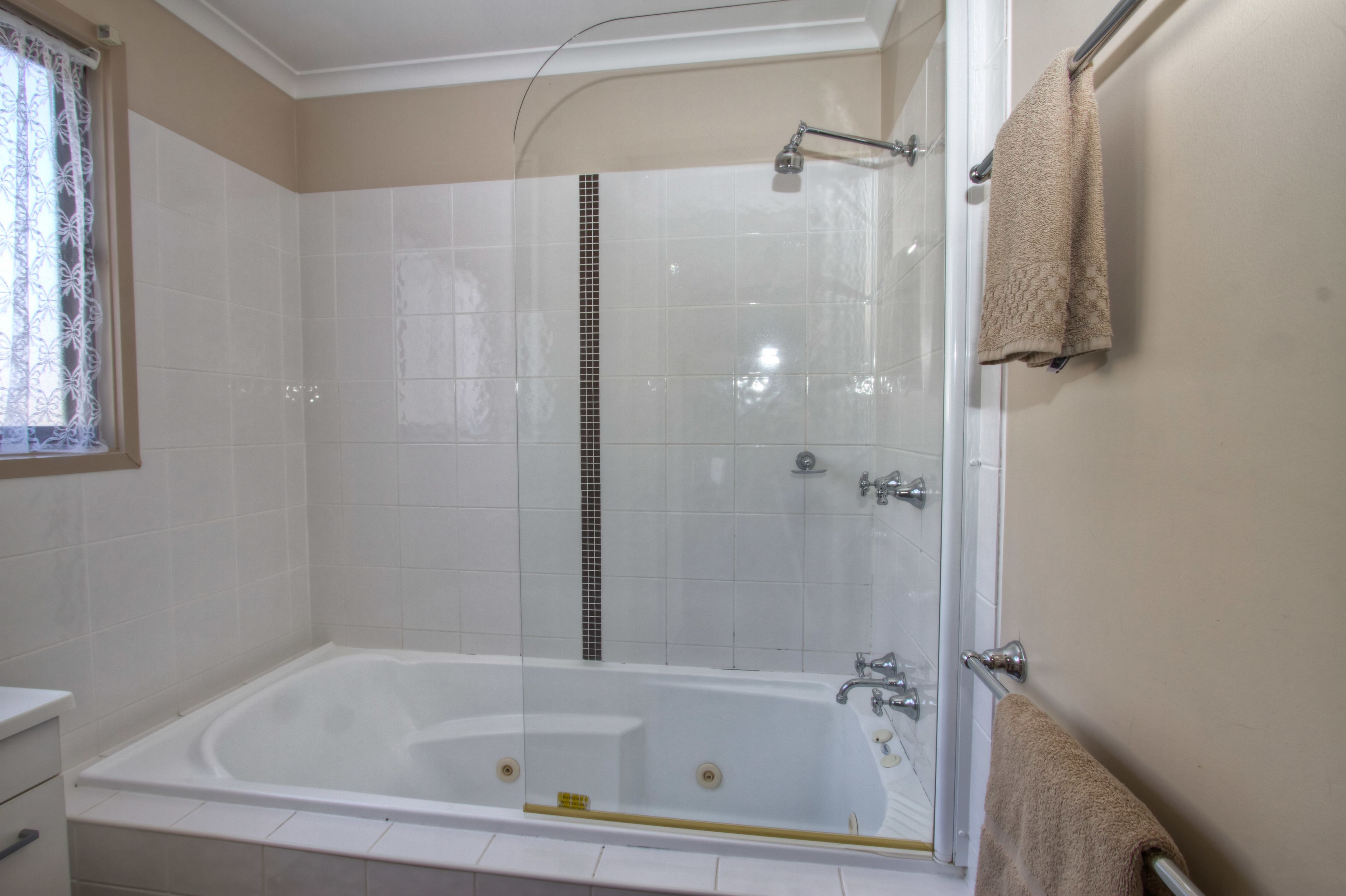 A modern bathroom with a glass-enclosed shower, a white bathtub, and beige walls.