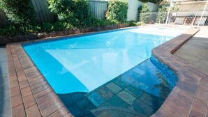 A swimming pool with a clear blue water surface, surrounded by a brick border and a stone edge.