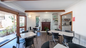 A dining area with tables and chairs, a fireplace, and a kitchen area visible through an open door.