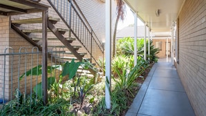 A covered outdoor corridor with a brick wall, metal staircase, and potted plants.